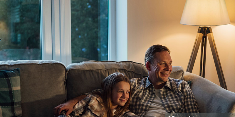 Father and daughter relaxing on couch with warm light, cozy ambiance