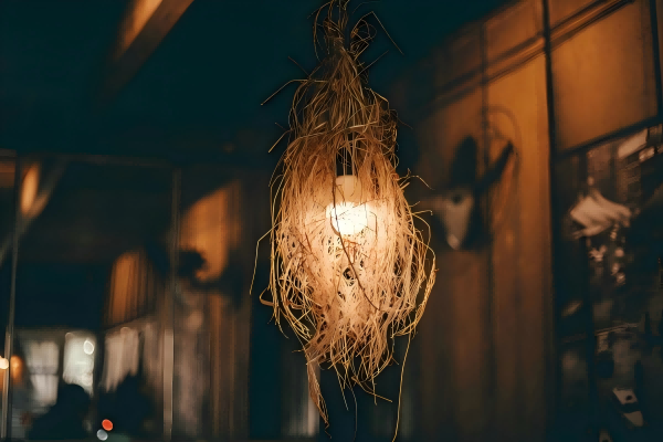 Rustic hanging light bulb wrapped in natural straw, casting a warm glow in a cozy interior setting.