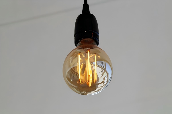 Minimalist LED filament bulb glowing warmly, suspended against a clean white background.