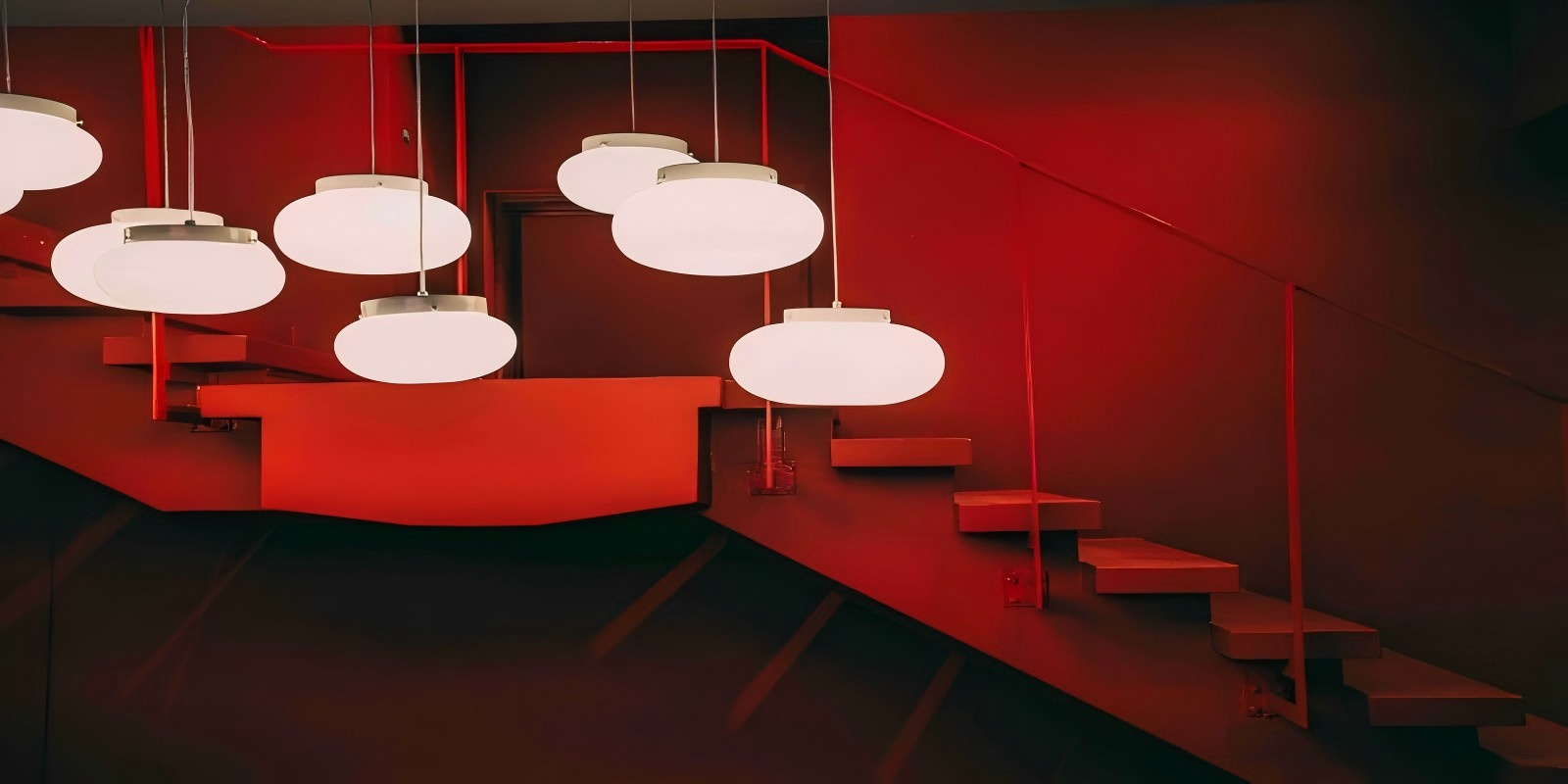 Contemporary pendant lights with a red backdrop, modern staircase lighting.