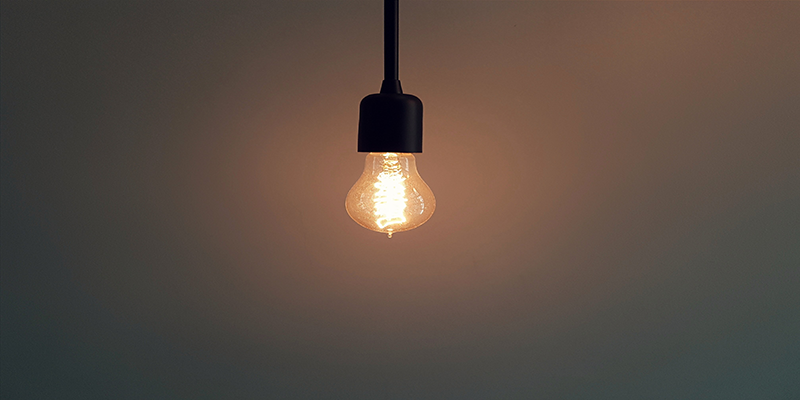 Minimalist LED filament bulb hanging from a ceiling, warm ambient lighting