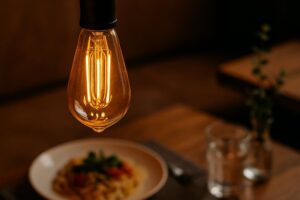 Close-up of glowing amber LED Edison bulb illuminating a restaurant table setting with food and decor details