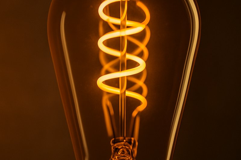 Close-up shot meticulously showcasing the intricate filament design of an amber-tinted ST64 LED Edison bulb, highlighting its warm aesthetic and craftsmanship.