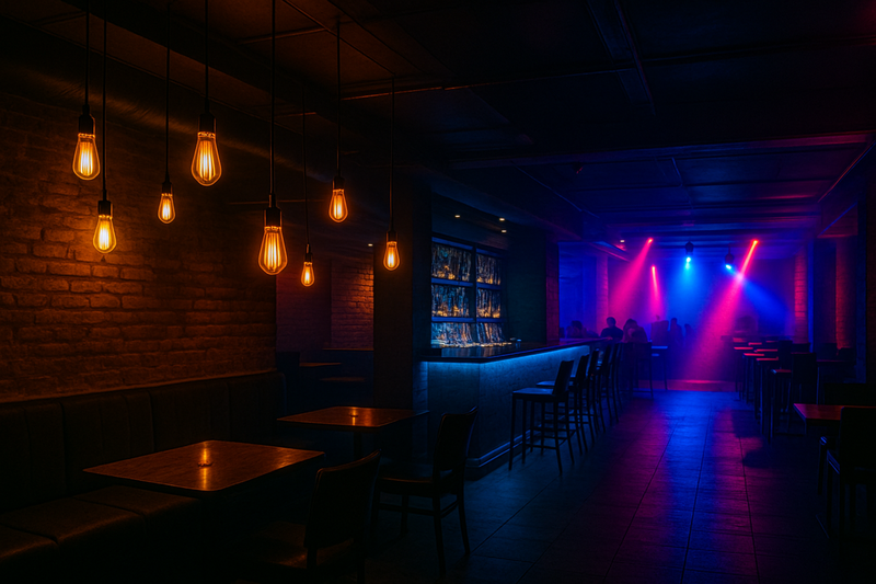 A nightclub interior showing distinct lighting zones: a softly lit lounge area with LED Edison bulbs, a brighter bar area, and dynamic lighting near a dance floor.
